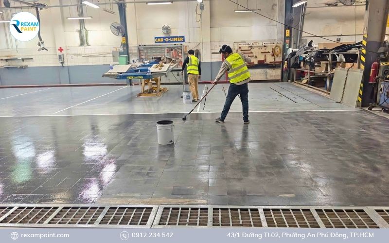 Thợ thi công lăn lớp sơn phủ epoxy màu xám lên mặt sàn gạch đã xử lý