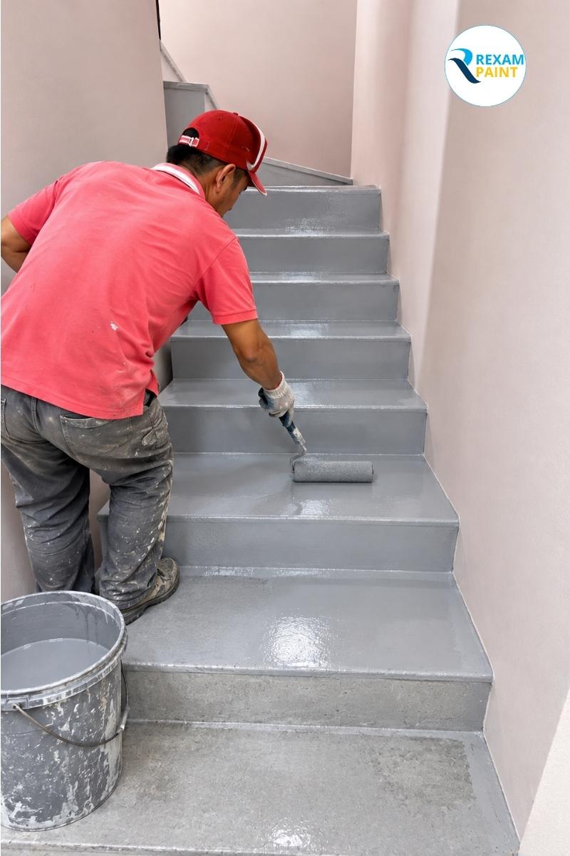 Thợ thi công lăn sơn epoxy lên từng bậc cầu thang bê tông theo hướng từ trên xuống