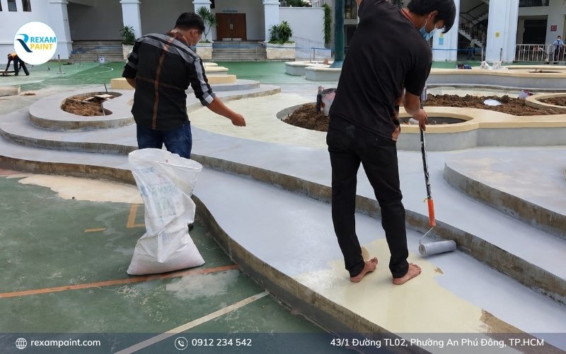 Thợ thi công rắc cốt liệu tạo nhám lên lớp sơn epoxy còn ướt
