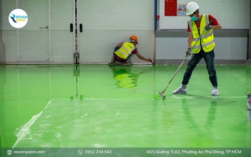 Thợ dùng bàn cào răng cưa kéo lớp sơn epoxy tự san phẳng trên sàn nhà xưởng